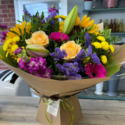Sunshine Surprise - A bold and joyful hand-tied bouquet featuring sunflowers, peach roses, lilac stock, gerbera, and bright yellow button chrysanthemums. A guaranteed day-brightener in a kraft box. Sunshine Surprise - A bold and joyful hand-tied bouquet featuring sunflowers, peach roses, lilac stock, gerbera, and bright yellow button chrysanthemums. A guaranteed day-brightener in a kraft box.